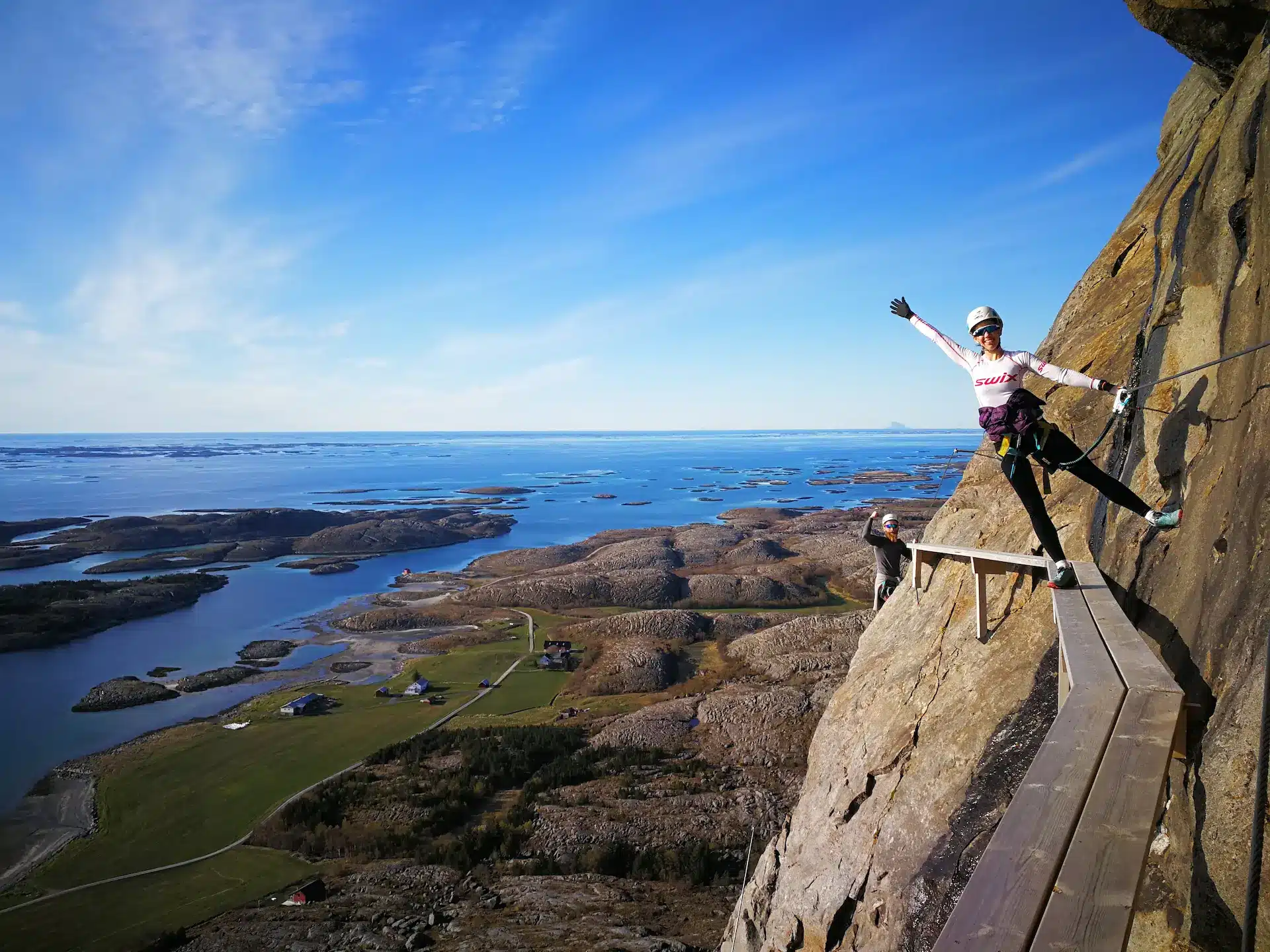 En blid person som klatrer Ravnfloget Via Ferrata på Helgelandskysten med blå himmel og nydelig natur i bakgrunnen